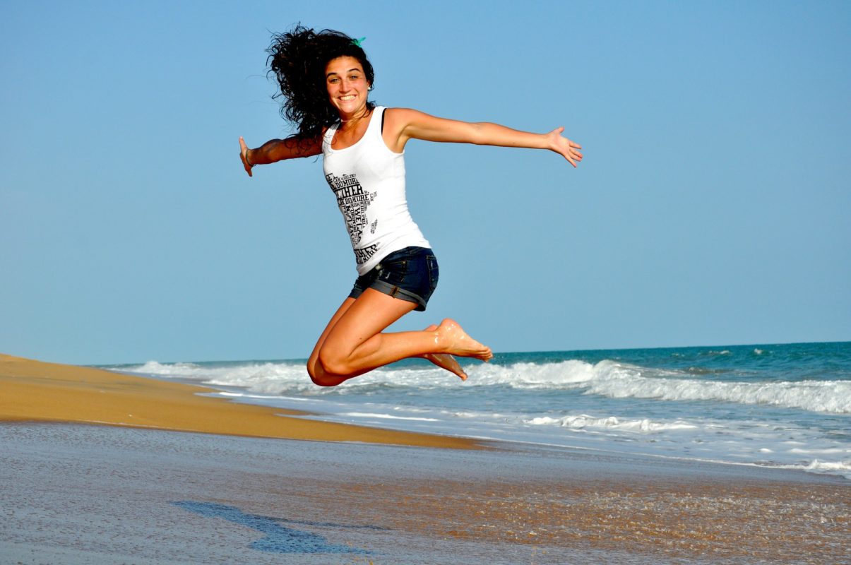 Femme qui saute de joie sur le sable devant la mer